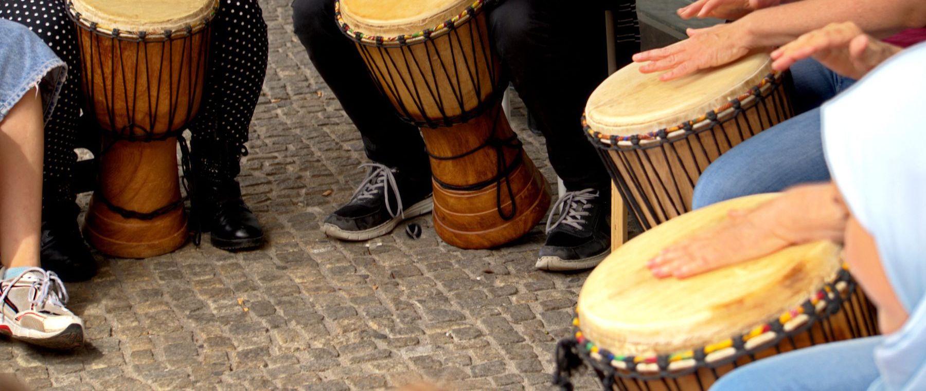 A circle of people playing djembe drums together outdoors